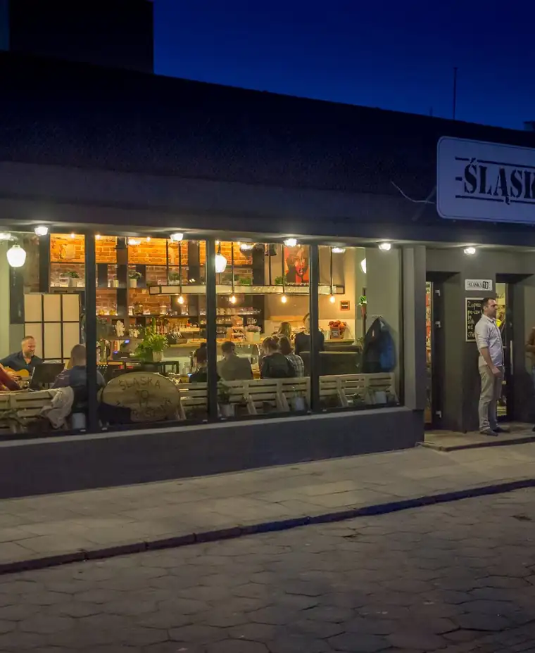 Restauracja Śląska 19 wieczorem — oświetlone okna i szyld na rogu bloku